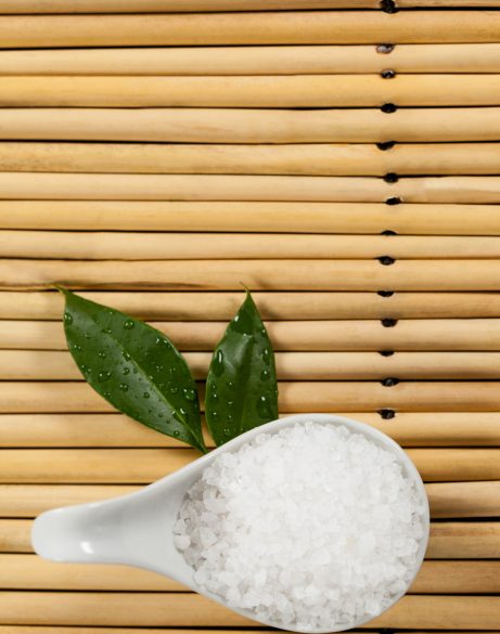 Two green leaves and sea salt in spoon on bamboo mat